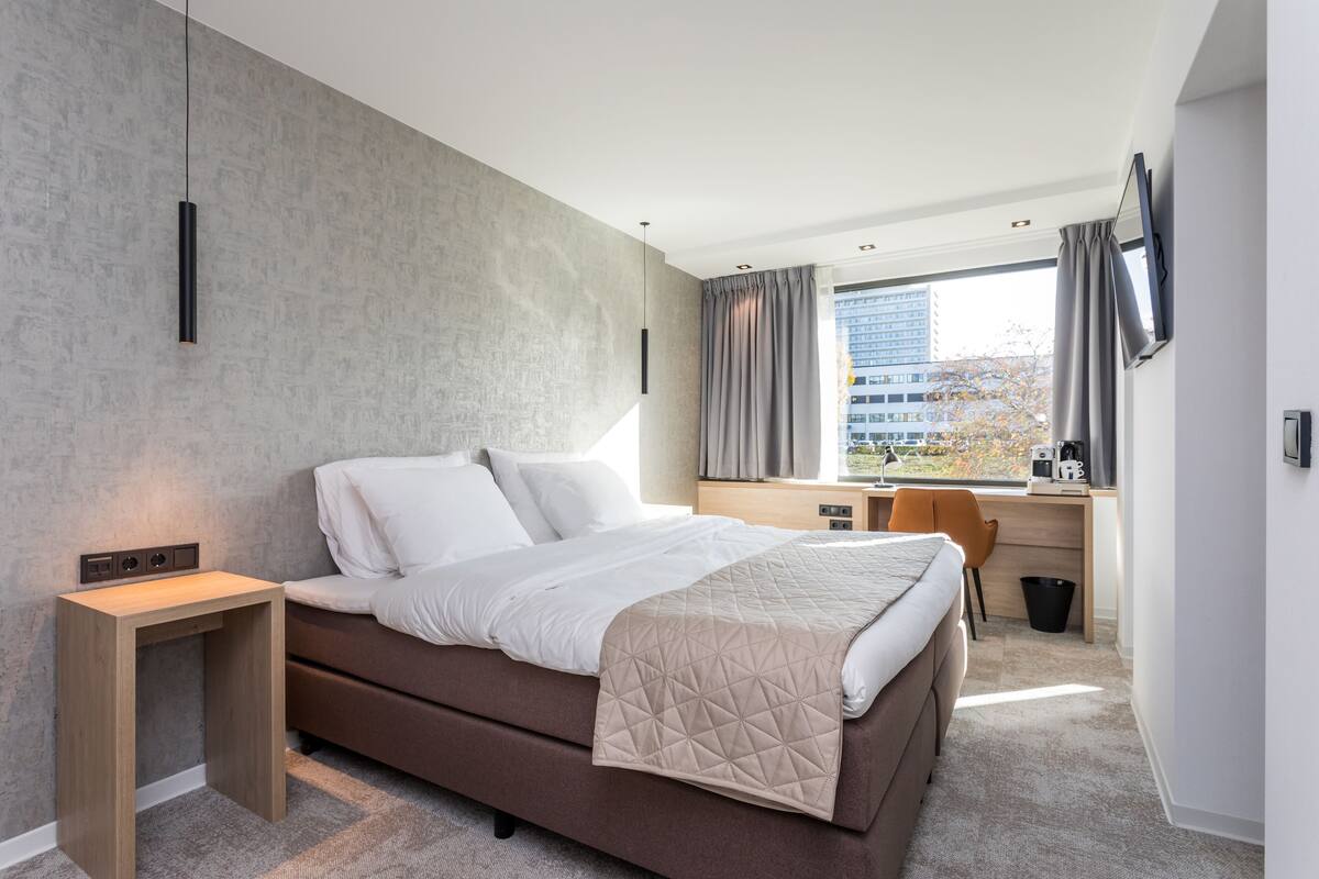Una habitación de hotel moderna con una cama grande, un escritorio y vistas a la ciudad.