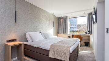A modern hotel room with a large bed, a desk, and a view of the city.
