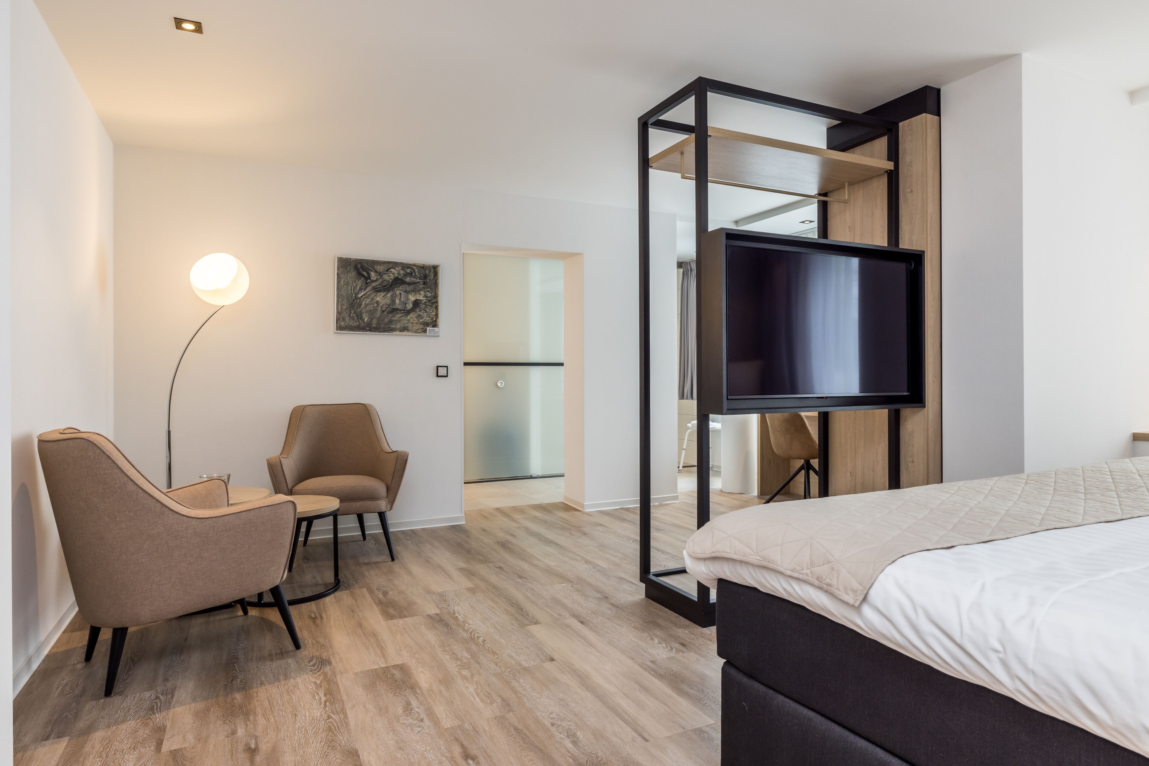 Una habitación de hotel moderna con cama, escritorio, silla, televisión y puerta de vidrio que da al baño.
