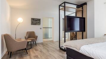 Una habitación de hotel moderna con cama, escritorio, silla, televisión y puerta de vidrio que da al baño.