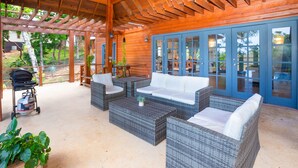 Un patio exterior con mobiliario de mimbre, una parrilla y vistas del entorno verde.