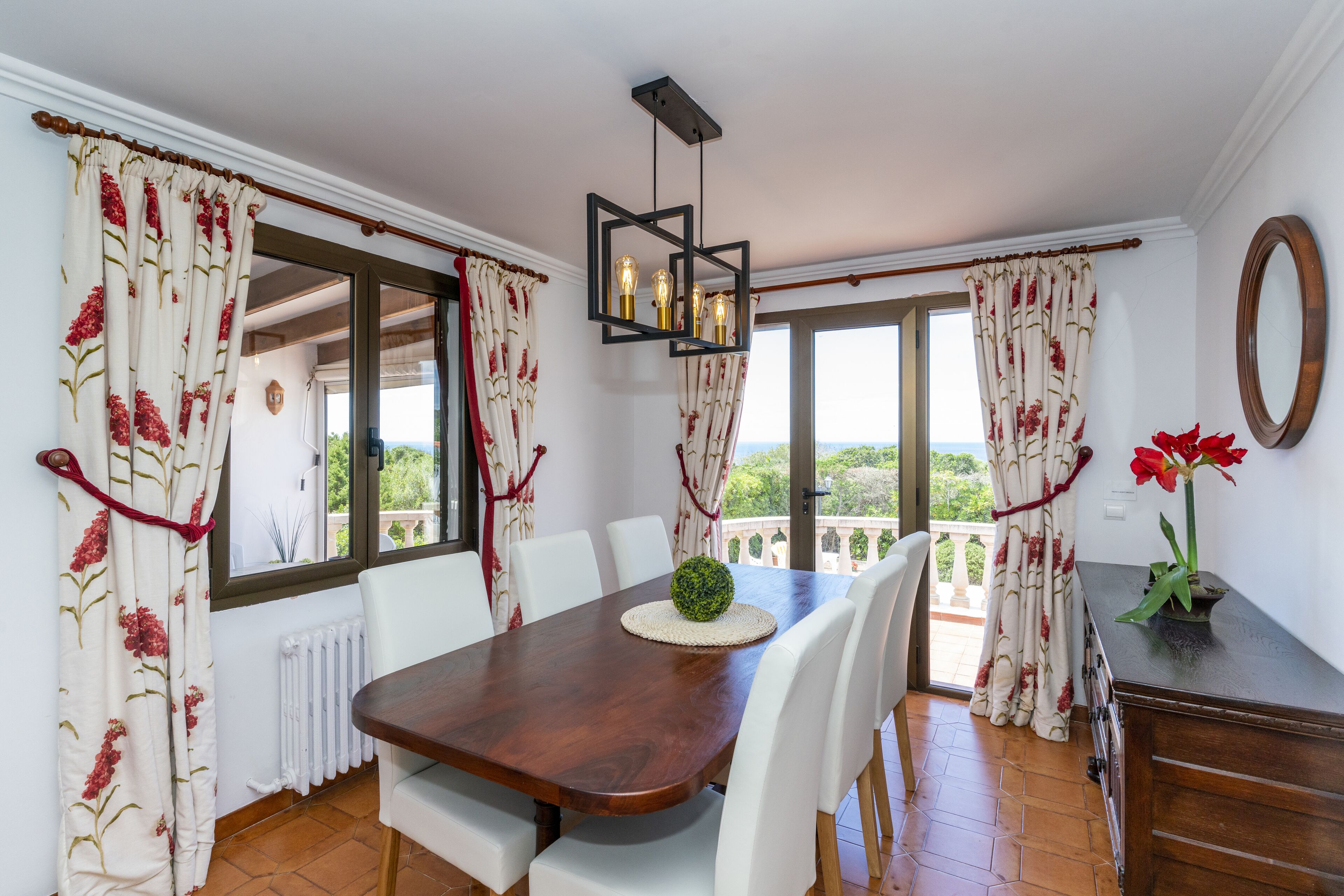 A dining area with a wooden table, white chairs, and a view through large windows.