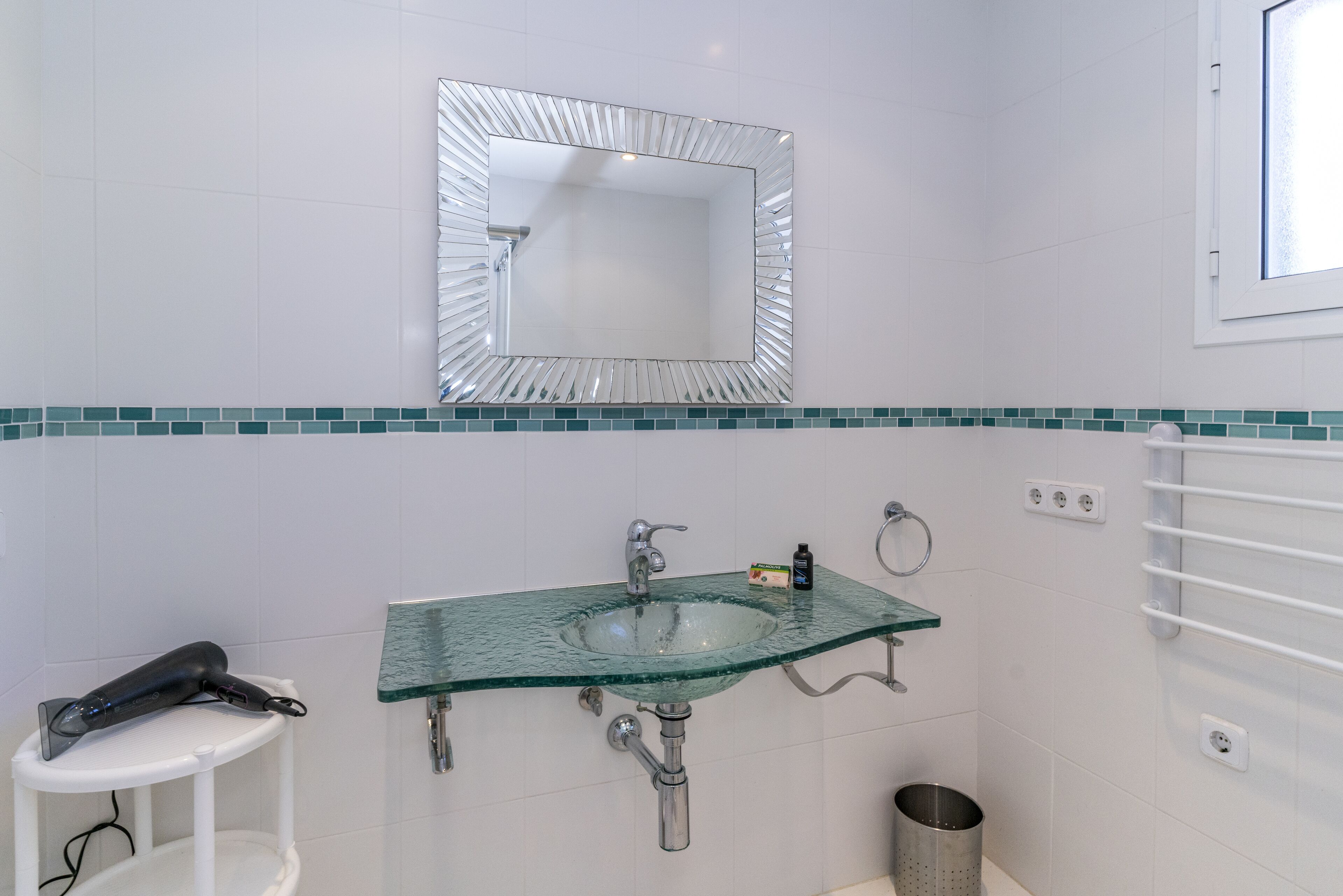 A bathroom with a glass sink, a mirror, and a hairdryer on a small table.