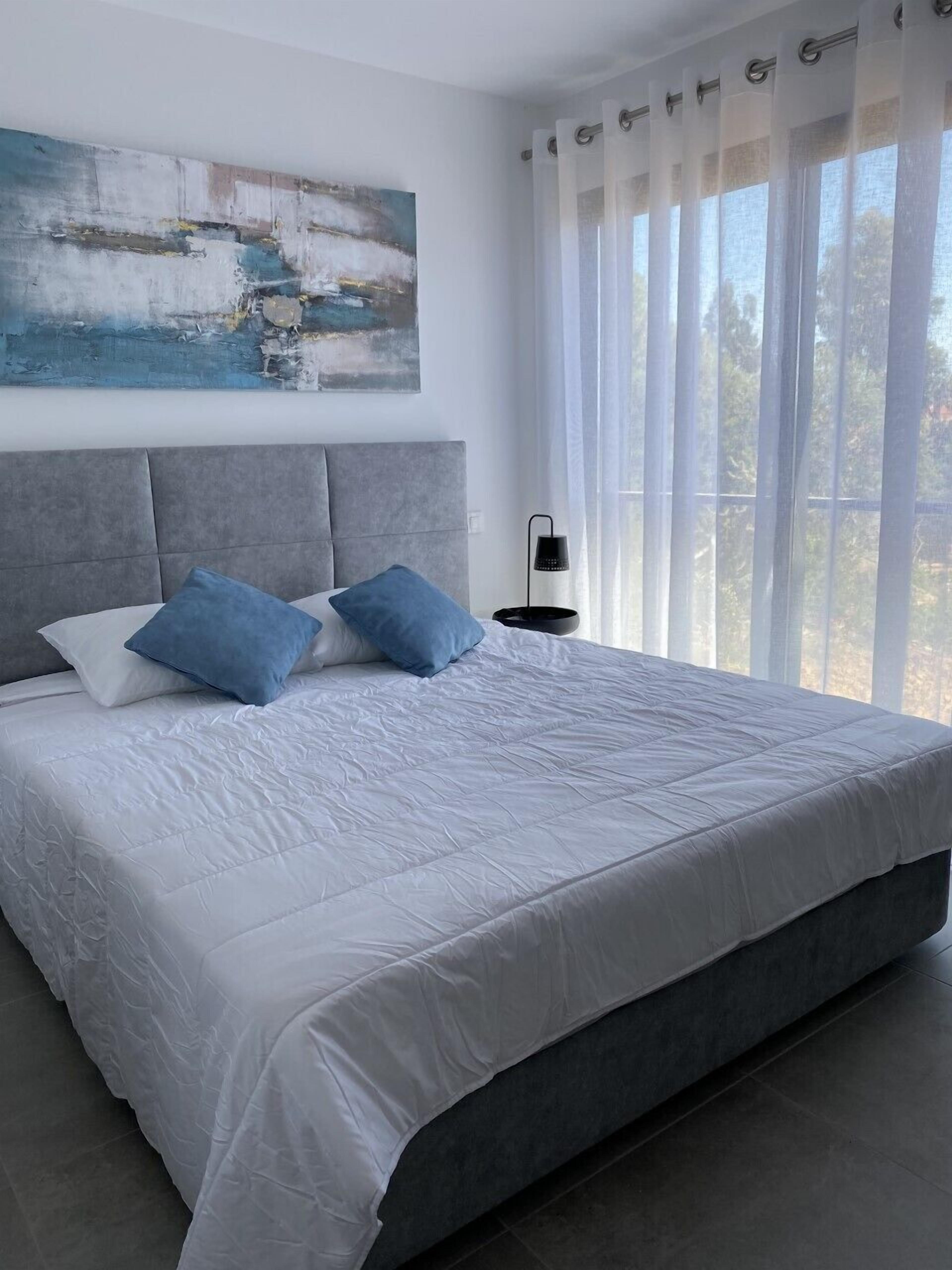 A modern bedroom with a large bed, grey headboard, and blue pillows.