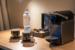 Een koffieapparaat, twee kopjes en een waterfles op een houten tafel.