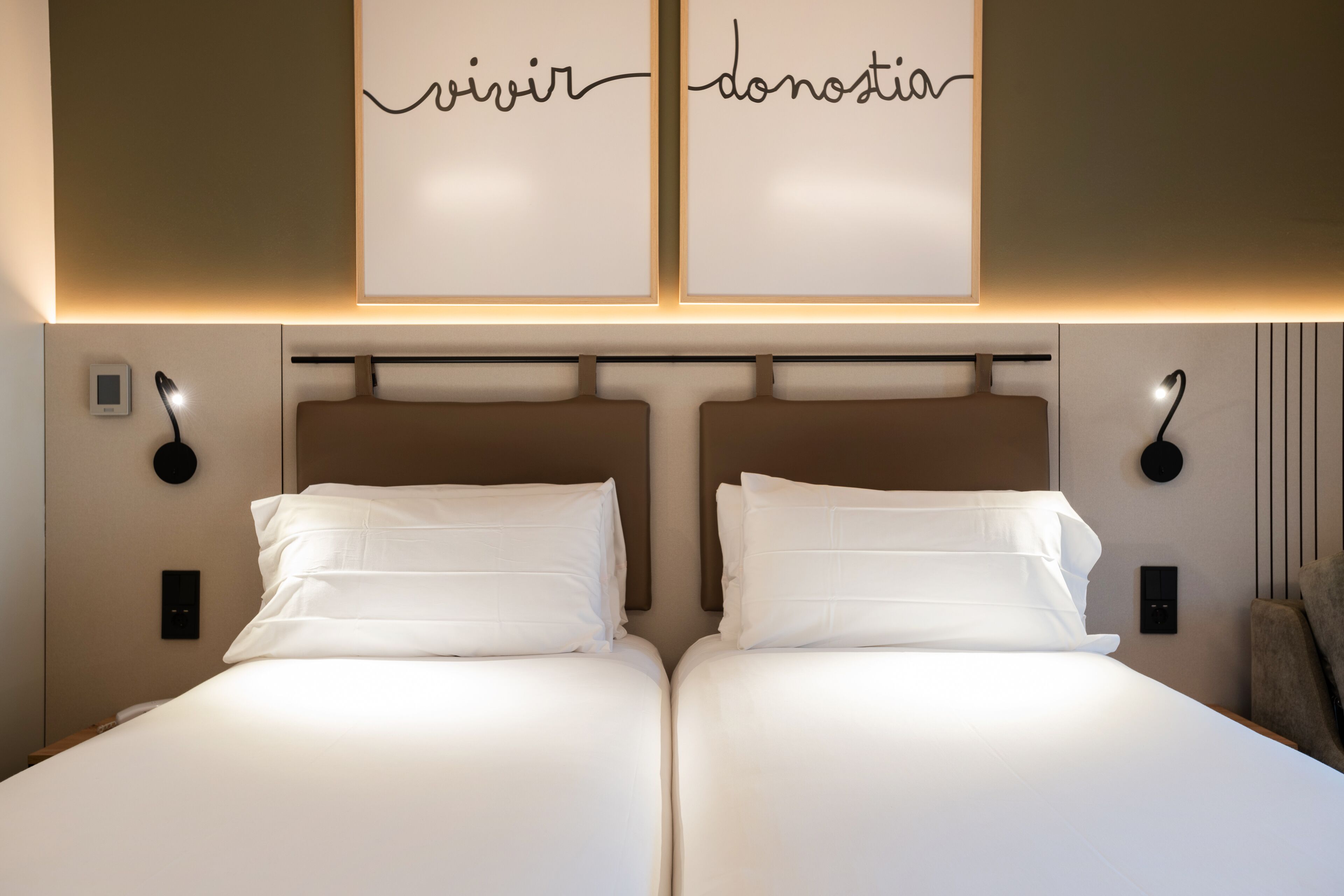 Una cama doble con ropa de cama blanca, dos mesitas de noche con lámparas y un aplique de pared.