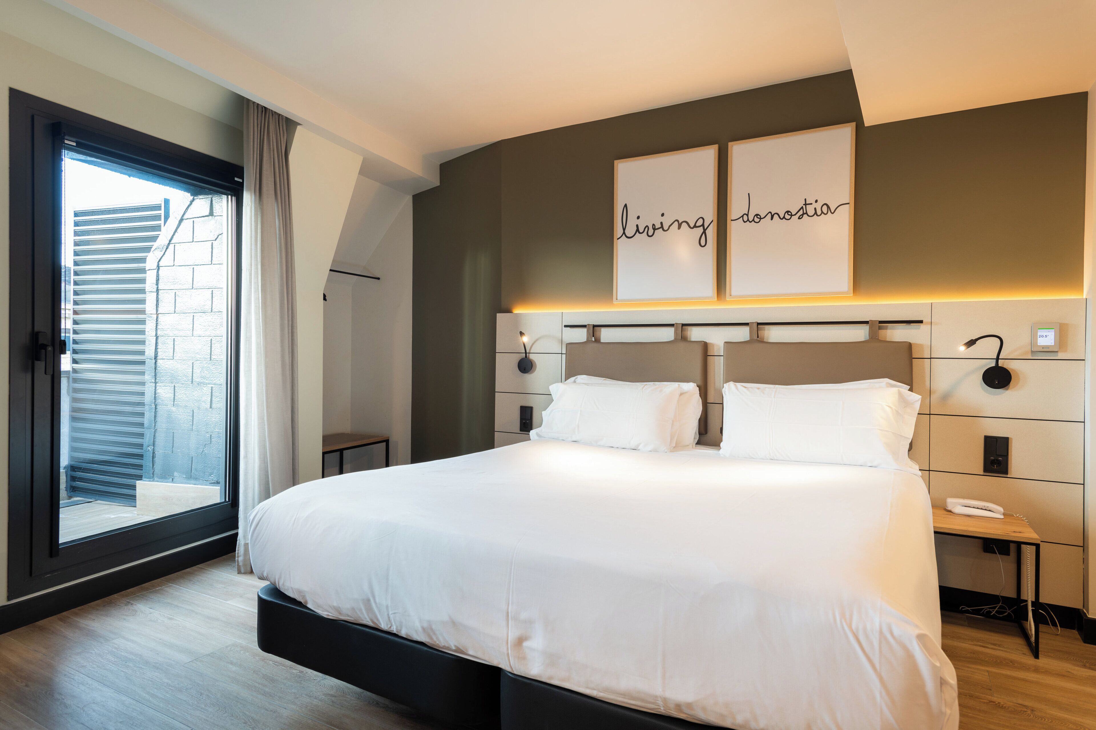 A modern hotel room with a large bed, a sliding glass door to the balcony, and a wall-mounted artwork.