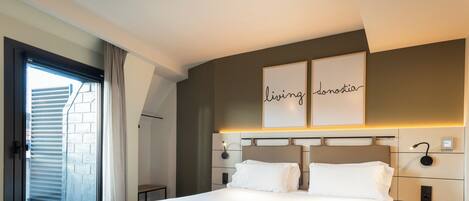 A modern hotel room with a large bed, a sliding glass door to the balcony, and a wall-mounted artwork.