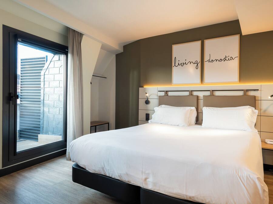 Una habitación de hotel moderna con una cama grande, una puerta corrediza al balcón y una obra de arte colgada en la pared.
