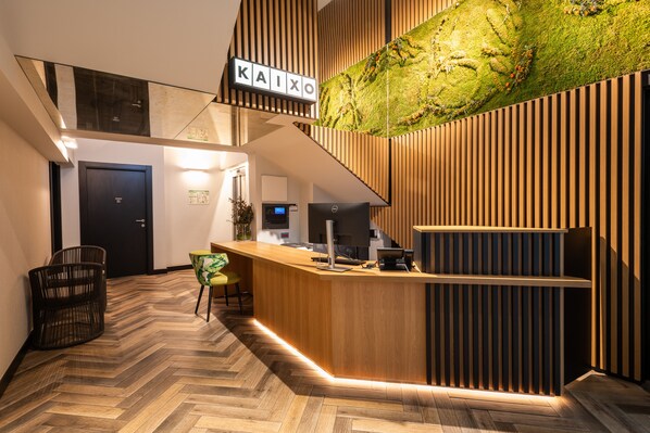 Een moderne receptie met een houten receptiebalie, een visgraatvloer en een wand van verticale houten panelen.