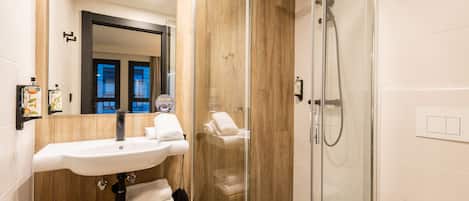 A modern bathroom with a glass-enclosed shower, a white sink with a wooden countertop, and a mirror above the sink.