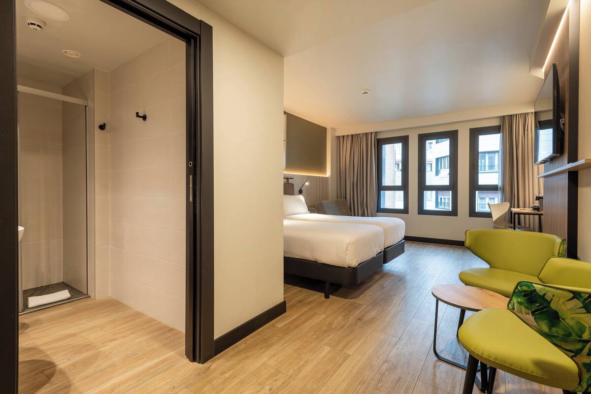 Een hotelkamer met een bed, een groene fauteuil en een bureau.