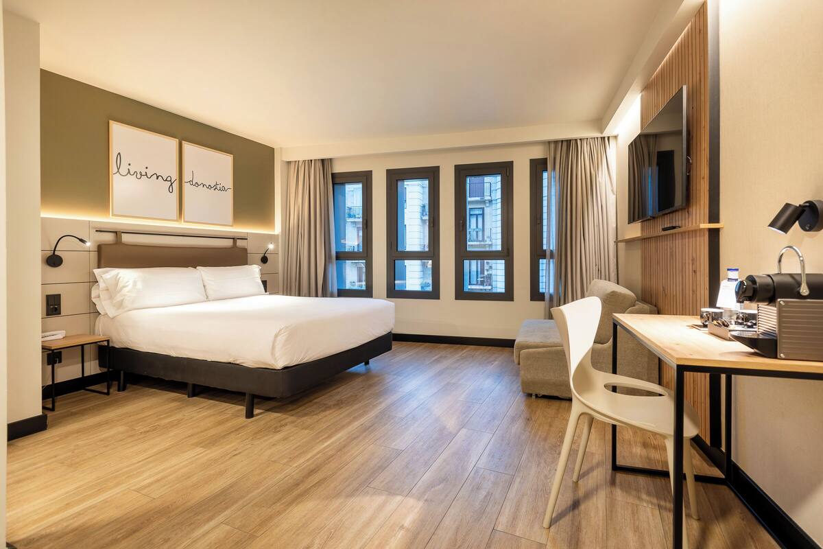 Een hotelkamer met een bed, bureau, stoel en grote ramen.