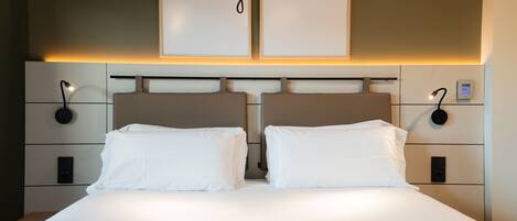 A hotel room with a large bed, two bedside tables with lamps, a wall-mounted control panel, and a sign above the bed reading "living donostia".