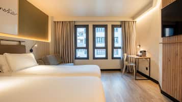 A hotel room with two beds, a desk, a chair, and a TV.