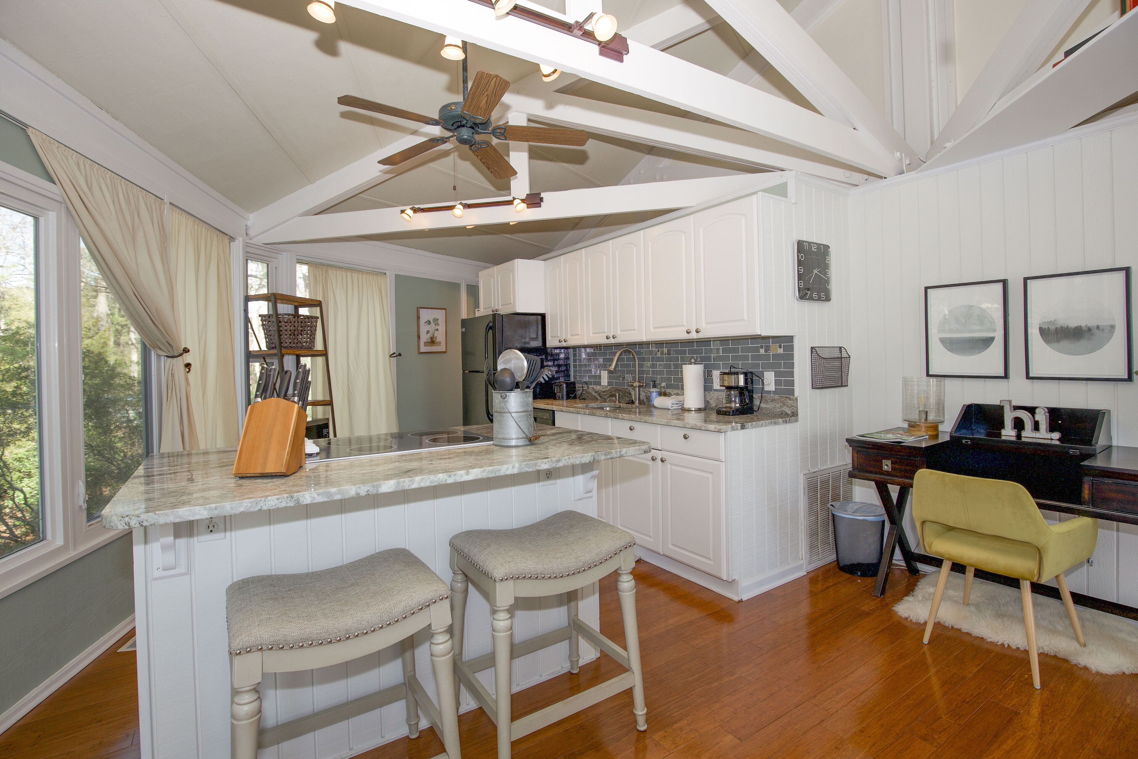 A kitchen with white cabinets, a marble countertop, a ceiling fan, and a wooden floor.