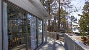Une terrasse en bois couverte, dotée de portes vitrées donnant sur une pièce, et entourée d’arbres, avec vue sur une étendue d’eau.
