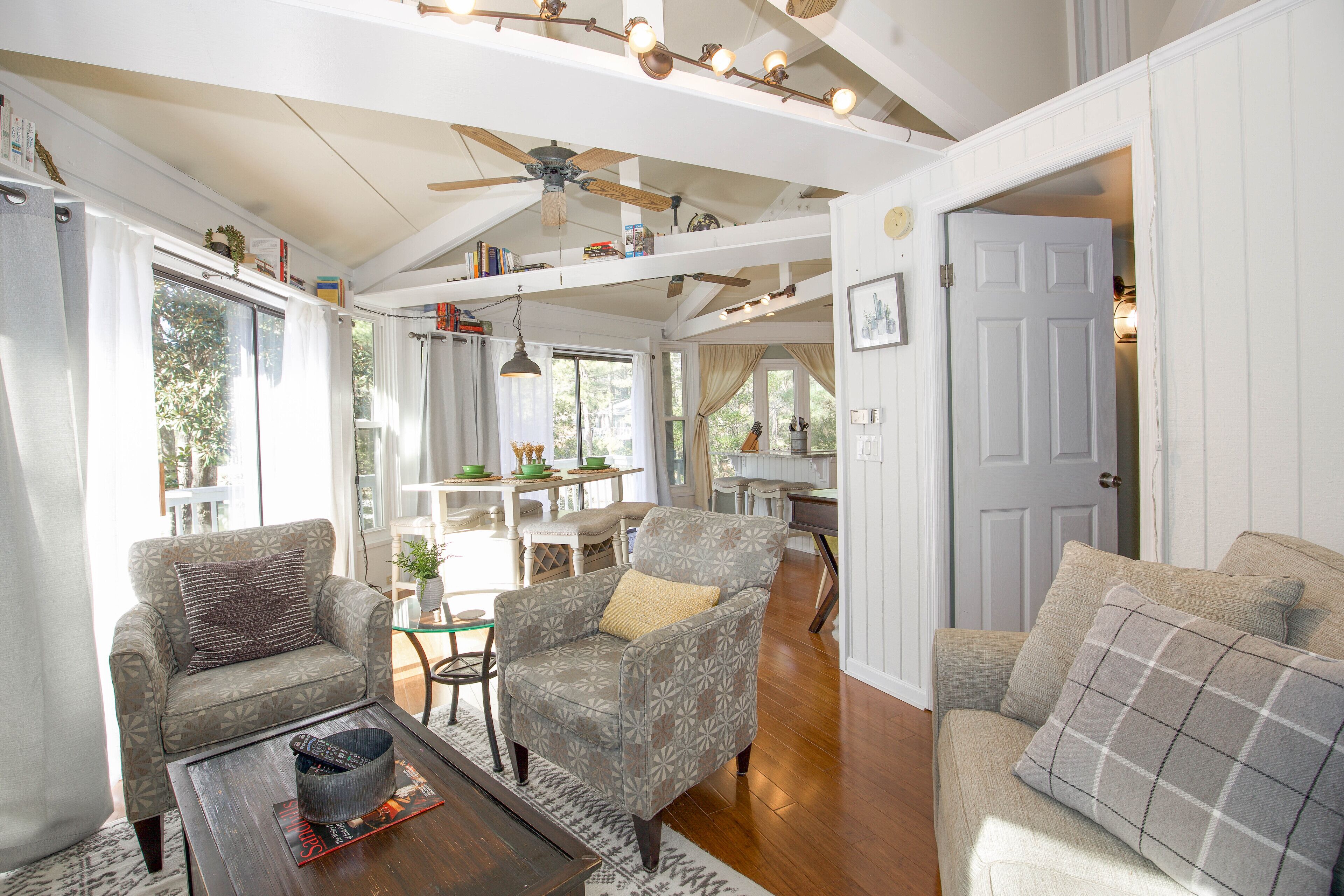 A spacious living room with a ceiling fan, a dining area with a table and chairs, and a door leading to another room.