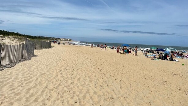 A sandy beach with a fence on one side and umbrellas and people on the other. - Renovated & Spacious Retreat on East Rt 1 – Pool, Bike Trails, Mins to Beach! (Lewes)