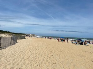 A sandy beach with a fence on one side and umbrellas and people on the other. - Renovated & Spacious Retreat on East Rt 1 – Pool, Bike Trails, Mins to Beach! (Lewes)
