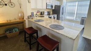 A kitchen with white cabinets, a granite countertop, a bicycle decoration, and a window with blinds. - Renovated & Spacious Retreat on East Rt 1 – Pool, Bike Trails, Mins to Beach! (Lewes)