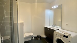 Un baño moderno con cabina de ducha de vidrio, inodoro, lavabo, espejo y lavadora de carga frontal.