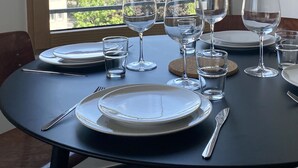 Mesa de comedor para seis personas, con copas de vino, platos y cubiertos, ubicada cerca de una ventana que ofrece vistas a árboles y edificios.