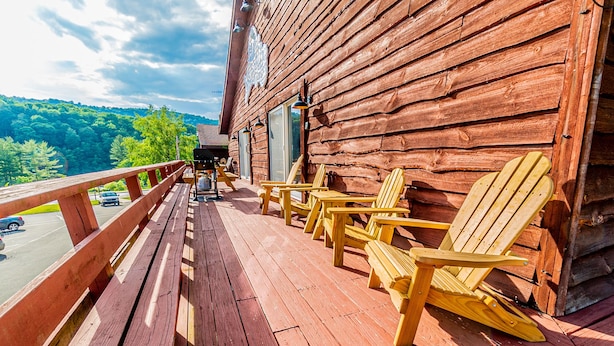Een houten terras met Adirondack-stoelen en een barbecue, met uitzicht op een bebost gebied.