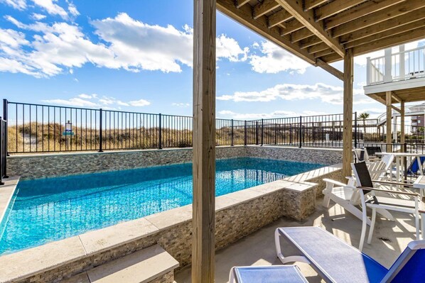 A swimming pool with a stone border, surrounded by lounge chairs and a wooden deck.