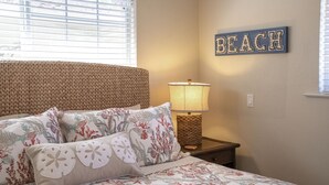 A bedroom with a bed, decorative pillows, a lamp, and a wall sign that reads "BEACH". - 3827 Betsy's Nest - Adorable Monterey Cottage (Monterey)