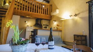 A cozy dining area with a table set for two, featuring a bottle of wine, two glasses, and a basket of flowers. A wooden staircase and a microwave are visible in the background. - Charming gîte in the heart of the vineyards - Swimming pool, Jacuzzi & Air conditioning (Fressac)