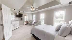 Une chambre à coucher avec un grand lit, un ventilateur de plafond, une télévision, une commode et une chaise.