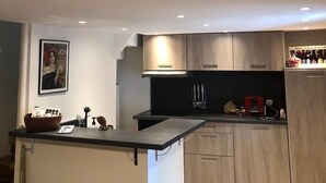 A modern kitchen with wooden cabinets, a black countertop, and recessed lighting. - Charmante Maison Avec Toit Terrasse (Montalba-le-Château)