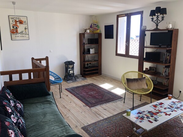 A cozy living room with a wooden sofa, a blue chair, a wooden bookshelf, a small table with a board game, and a decorative lamp.