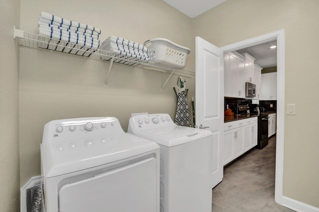 A laundry area with two front-loading washers and dryers, a shelf with folded towels, and a basket.