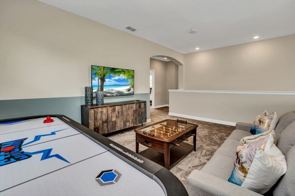A living room with a shuffleboard table, a foosball table, and a painting of a beach scene.