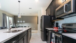 A modern kitchen with dark cabinetry, stainless steel appliances, and a marble floor. - Luxury Champions Gate Town Home 4 Bedroom Townhouse by RedAwning (Davenport)