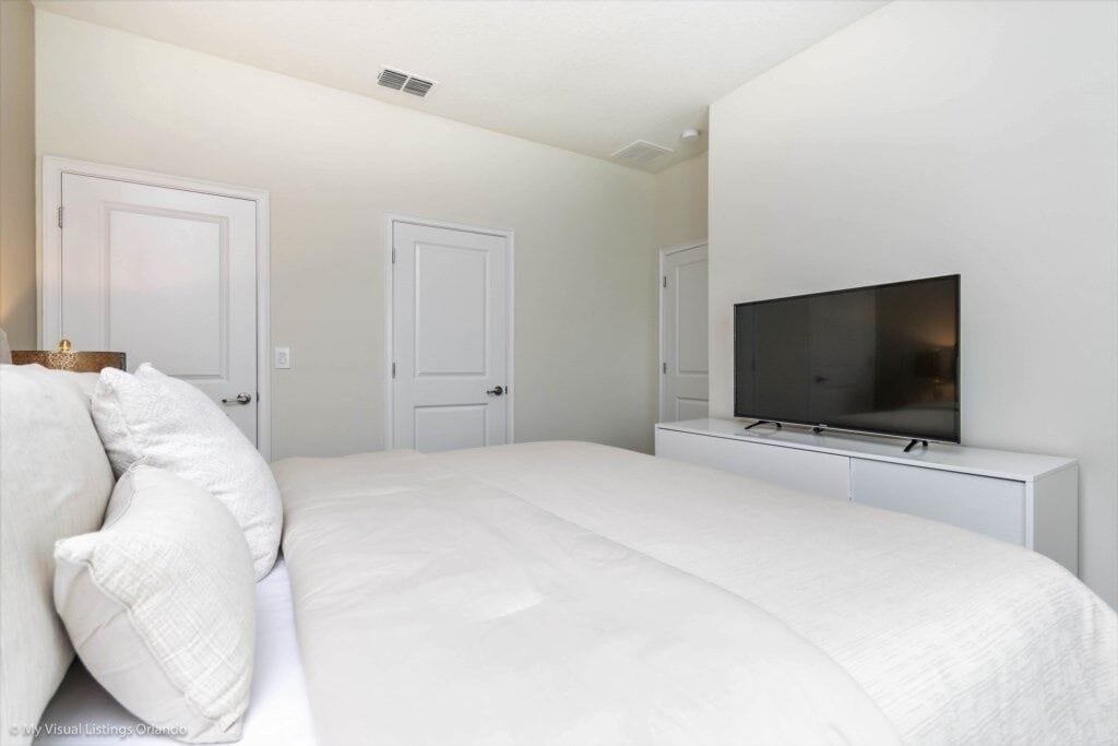 Un dormitorio con una cama, un televisor sobre un mueble y dos puertas.