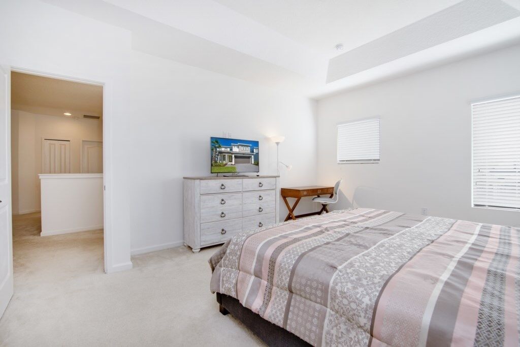 A bedroom with a bed, a dresser, a desk, and a window with blinds.