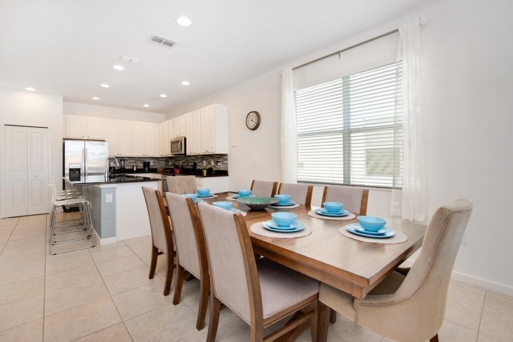 A modern kitchen with white cabinets, a central island, and a dining area with a wooden table set for six.