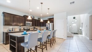 A modern kitchen with dark wood cabinets, a large island with bar stools, stainless steel appliances, and pendant lighting. - 8 Bed Windsor At Westside Resort! 8 Bedroom Villa by RedAwning (Kissimmee)