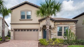 A two-story house with a beige facade, a stone accent wall, a garage, and a palm tree in the front yard. - 8 Bed Windsor At Westside Resort! 8 Bedroom Villa by RedAwning (Kissimmee)