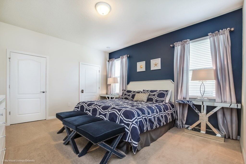 A bedroom with a bed, bench, bedside table, and curtains.