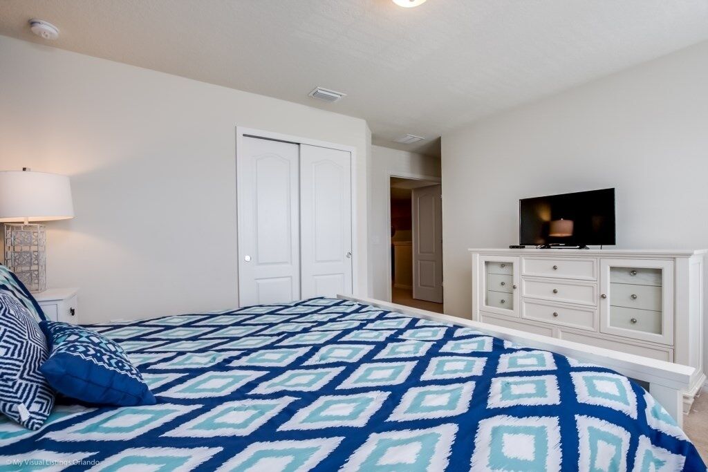 A bedroom with a bed, a television on a dresser, and a door leading to another room.