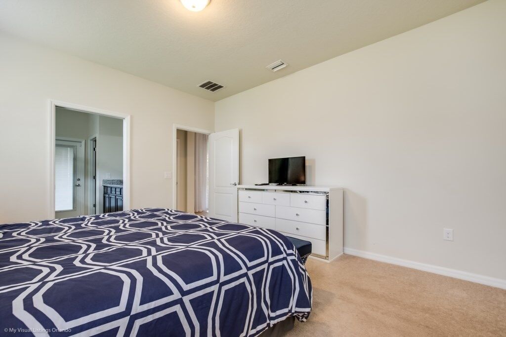 A bedroom with a large bed, a dresser, and a television on top.