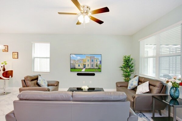A modern living room with a ceiling fan, two sofas, a coffee table, and a TV mounted on the wall.