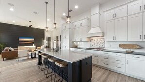 A modern kitchen with white cabinets, a large island with bar stools, and pendant lighting.