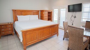 A bedroom with a large wooden bed, a nightstand, a dresser, a wicker chair, a television mounted on the wall, and a sliding glass door leading to an outdoor area.