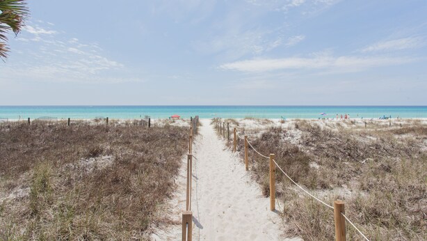 A sandy beach path leading to the ocean, surrounded by dunes and a wooden fence.