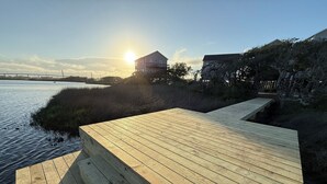 A wooden deck extending over a body of water with a bridge in the background and a house on the right. - Waterfront: Dock Access, Walk to Beach, Pier & Shops, 5BR, Sunset view / 10% off (Surf City)